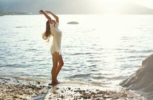 une femme dans une blanc robe permanent sur le plage photo