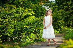 une peu fille dans une blanc robe en marchant sur une en bois chemin photo