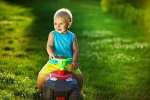 une Jeune garçon équitation une jouet voiture dans le herbe photo