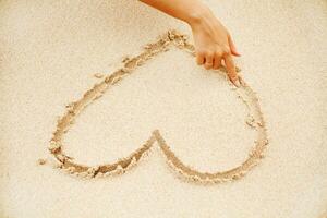 une main dessin une cœur dans le le sable photo
