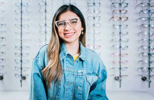 souriant content fille dans lunettes avec boutique lunettes arrière-plan, portrait de content fille dans des lunettes dans un lunettes boutique photo