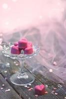 pralines au chocolat rose en forme de coeur, dans une belle cloche en verre, sur fond de bois blanc avec espace pour copie