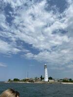 blanc phare. vue de mer à baie avec phare. magnifique nuageux ciels. Résidentiel bâtiments sur rivage. touristes tête sur premier plan photo