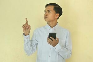 une homme montrer du doigt en haut en portant une mobile téléphone sur une Jaune Contexte photo