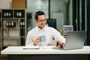 sur de soi asiatique homme avec une sourire permanent en portant bloc-notes et tablette à le bureau. photo