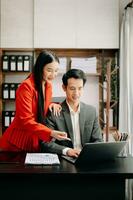 un collègue d'affaires asiatique présente et explique et utilise un ordinateur portable et une tablette. travail d'équipe, équipe de marketing financier, assis dans la salle de bureau. photo