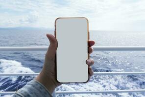 maquette image de une femme main en portant blanc mobile téléphone avec Vide blanc écran sur le ferry-boat dans de face de le turquoise mer et ciel. photo