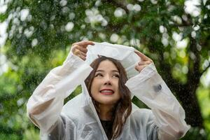 magnifique asiatique femme portant imperméable et profiter dans le pluie, pluvieux saison. photo
