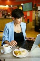 concentré femme avec nourriture et café travail sur portable dans café photo