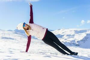 femme dans élégant des lunettes de protection avec côté planche yoga pose sur neigeux sol photo