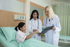 professionnel femelle médecins discuter et Explique radiographie film examen résultat à asiatique patient femme dans une hôpital quartier hospitalisé lit après soins de santé vérification et médical traitement. photo