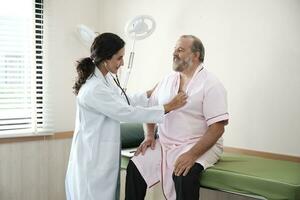 femelle médecins dans uniforme en bonne santé vérifier blanc Masculin les patients dans examen manteau par stéthoscope, et bilans et conseiller santé se soucier diagnostic à clinique hôpital, et rendez-vous visite. photo