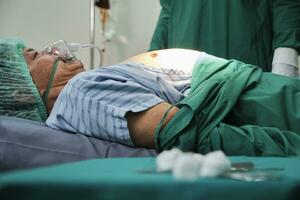 Masculin patient avec ventilateur sécurité la vie porter secours après urgence chirurgie, cpr en fonctionnement et médical de icu chirurgien médecins, santé restaurer sur de façon critique lit se soucier dans hôpital. photo