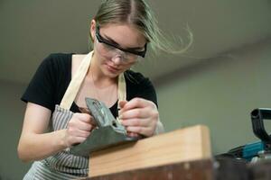 travailleur Charpentier femme en utilisant outils souriant en toute confiance Jeune femelle menuisier dans tablier permanent près Table de travail travail dans le artisanat atelier photo