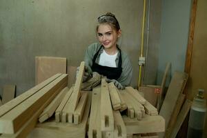 travailleur Charpentier femme en utilisant outils souriant en toute confiance Jeune femelle menuisier dans tablier permanent près Table de travail et à la recherche à caméra amical tandis que travail dans le artisanat atelier photo