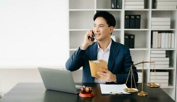 asiatique Masculin avocat bavardage en ligne avec client sur ordinateur portable, téléphone intelligent discuter détails de procès. dans Bureau photo