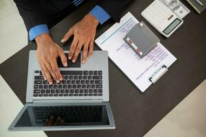 réel biens agent est assis et chèques client information avec portable ordinateur situé sur bureau dans Bureau avant qui passe information à la finance entreprise dans commande à prêter leur prêt à acheter réel domaine. photo