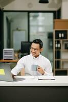 sur de soi asiatique homme avec une sourire permanent en portant bloc-notes et tablette à le bureau. photo