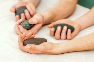 quatre mains de Masculin masseurs en portant spa des pierres sur blanc serviette Haut voir. pierre massage concept. photo