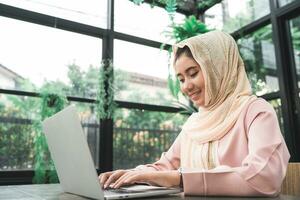 belle jeune femme musulmane asiatique souriante travaillant sur ordinateur portable assis dans le salon à la maison. femme d'affaires asiatique document de travail finance et calculatrice dans son bureau à domicile. profiter du temps à la maison. photo