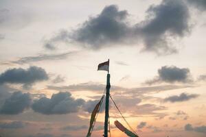 le bateau mât, sur Haut de lequel le indonésien drapeau est agitant, comme crépuscule arrive avec magnifique soir des nuages. photo