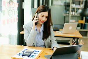 une femme d'affaires asiatique heureuse a la joie de parler sur le smartphone, la tablette et l'ordinateur portable du bureau moderne photo