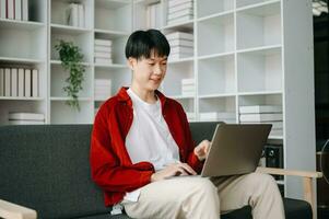 Jeune attrayant asiatique homme souriant en pensant Planification l'écriture dans carnet de notes, tablette et portable travail de Accueil à Accueil Bureau photo