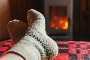 pieds jambes dans des chaussettes de laine de vêtements d'hiver au fond de la cheminée. femme assise à la maison le soir d'hiver ou d'automne se détendre et se réchauffer. concept d'hiver et de temps froid. réveillon de noël hygge. photo