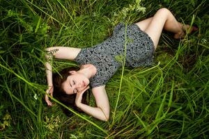 brunette femme mensonge sur vert herbe. beauté fille en plein air profiter la nature et relaxation. gratuit content femme, Haut vue photo