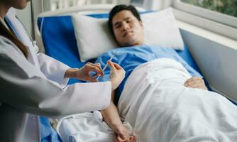 asiatique médecin dans blanc costume prendre Remarques tandis que discuter et asiatique âgé, homme patient qui mensonge sur lit avec recevoir saline Solution dans hôpital ou clinique. photo