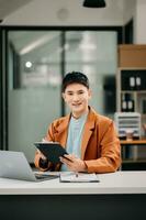 affaires asiatique homme parlant sur le téléphone et en utilisant une portable avec une sourire tandis que séance à moderne Bureau photo