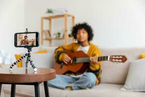 blogueur guitariste. content africain américain fille blogueur en jouant guitare en chantant chanson enregistrement vlog. social médias influenceur femme diffusion enregistrement à Accueil studio. la musique contenu créateur diffuser. photo