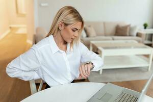 femme d'affaires frustrée au travail regardant la montre-bracelet. prêt à quitter le bureau. jeune femme ennuyée au bureau travaillant avec un ordinateur portable et regardant l'heure photo