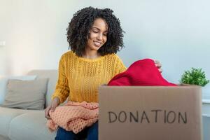 notion de don. femme tenant une boîte de dons pleine de vêtements. femme tenant un livre et une boîte de don de vêtements. vêtements dans une boîte pour le don de concept et le recyclage de réutilisation photo