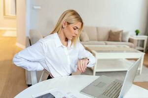 femme d'affaires frustrée au travail regardant la montre-bracelet. prêt à quitter le bureau. jeune femme ennuyée au bureau travaillant avec un ordinateur portable et regardant l'heure photo