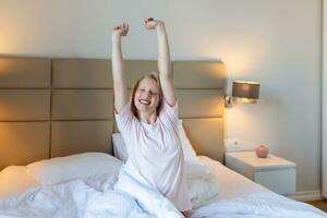 femme qui s'étend dans son lit avec ses bras levés. portrait d'une jolie fille charmante profitant du temps passé dans le mauvais après avoir dormi allongé sous une couverture faisant des étirements en gardant les yeux fermés. bonne santé photo