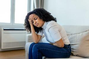 femme afro-américaine dans une expression douloureuse tenant la main contre le ventre souffrant de douleurs menstruelles, allongée triste sur son lit à la maison, ayant une crampe abdominale dans le concept de santé féminine photo