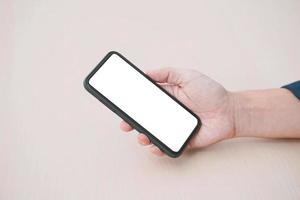 smartphone à écran blanc d'image de maquette. smartphone blanc vierge tenu par la main masculine sur fond en bois. photo