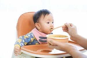 Petite fille de 6 mois mangeant des aliments mélangés sur une chaise haute. photo