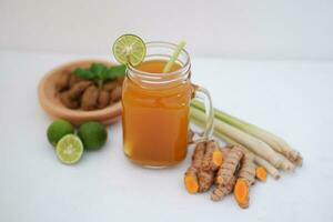 Frais gingembre et citron jus dans une verre pot avec gingembre les racines sur blanc Contexte. photo