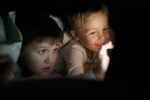deux garçons en train de regarder film ou dessin animé sur tampon à nuit photo