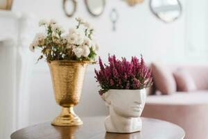 violet bruyère à le vase sculpture de une tête et blanc chrysanthèmes dans une d'or classique vase sur une table dans le intérieur de une confortable maison photo