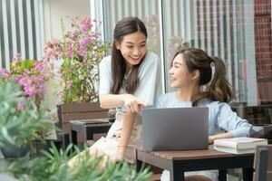 portrait de asiatique femelle meilleur ami séance en utilisant portable sur le balcon à l'extérieur le maison. deux content femmes tandis que achats en ligne ou fonctionnement. photo