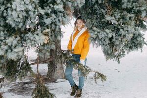 adolescent blond dans une Jaune chandail à l'extérieur dans l'hiver. une adolescent fille sur une marcher dans hiver vêtements dans une neigeux forêt photo