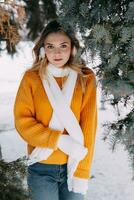 adolescent blond dans une Jaune chandail à l'extérieur dans l'hiver. une adolescent fille sur une marcher dans hiver vêtements dans une neigeux forêt photo