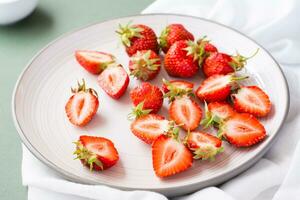 Frais entier et tranché des fraises sur une assiette sur une vert Contexte. été vitamine aliments. fermer photo