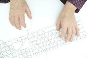 mains de un vieux femelle dactylographie sur le clavier et en utilisant souris, isolé sur blanc, fermer. photo