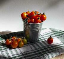Cerise tomates dans une seau sur une nappe de table en dessous de le Soleil photo