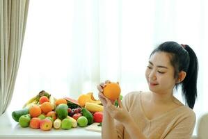 portrait femmes main tenant des fruits orange avec un assortiment de fruits et légumes mûrs frais sur la table à fond de rideau blanc photo