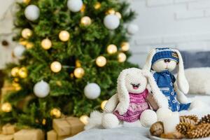 Fait main tricoté lapin. Noël lapin dans une écharpe et chapeau avec une grand pompon parmi le décoratif Noël des arbres et des balles. Noël composition photo